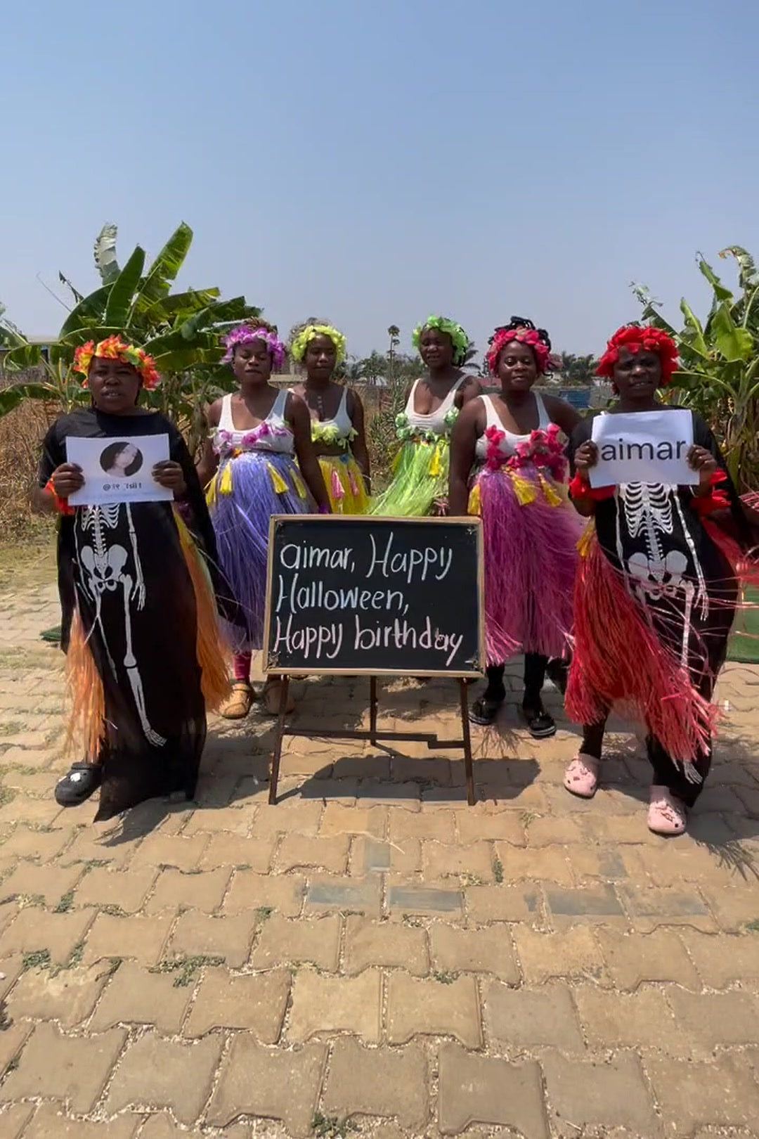 African Mamas crew in Halloween costume — skeleton dresses and flower crowns, holding a Happy Halloween Happy Birthday board